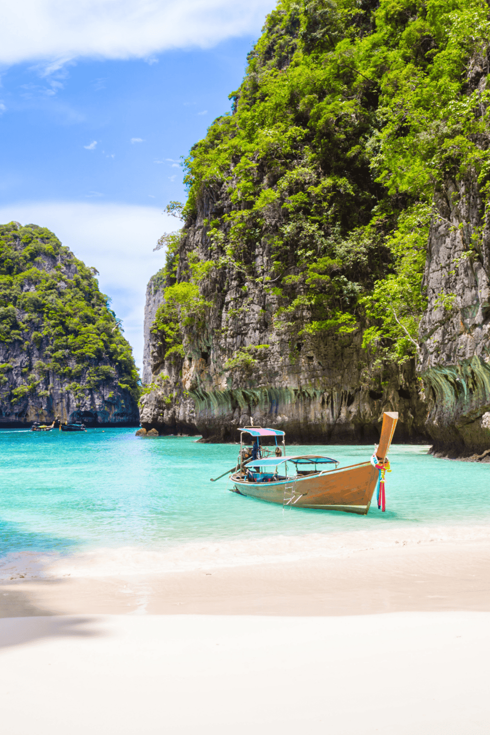 Vibrant tropical beach with turquoise water, limestone cliffs, and traditional longtail boat in Thailand.