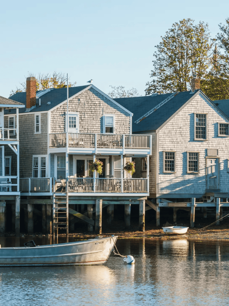 Waterside coastal house with wooden deck, boats, and trees, scenic waterfront with outdoor living space.