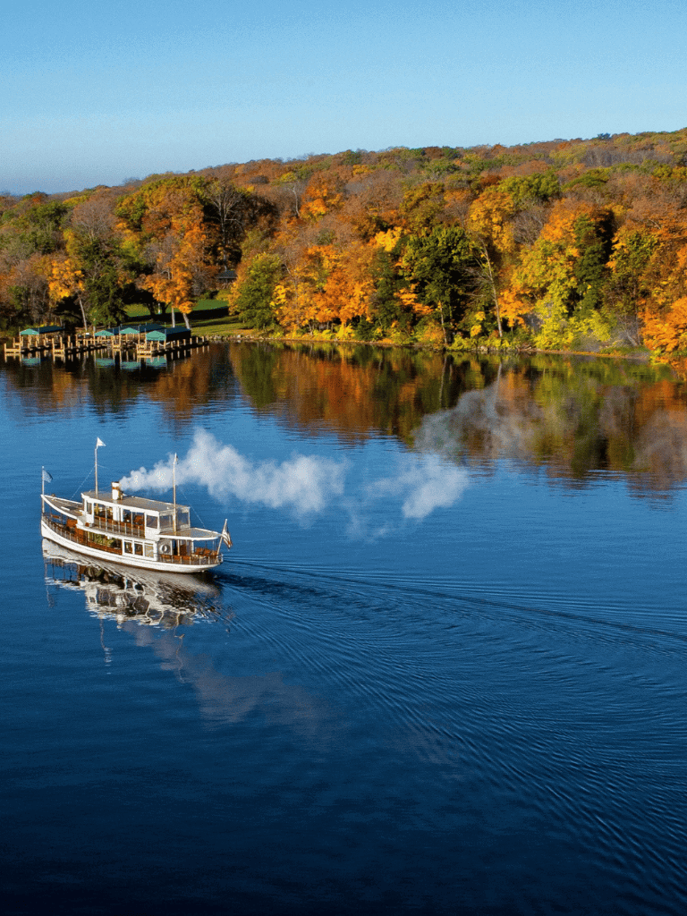 Colorful fall foliage along a lakeshore with a boat on the water.