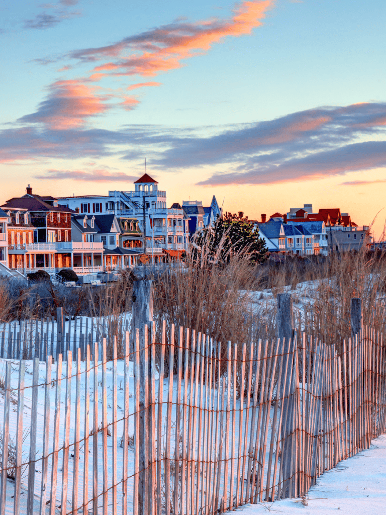 Colorful beach houses near sandy dunes with fencing at sunset, seaside vacation destination.