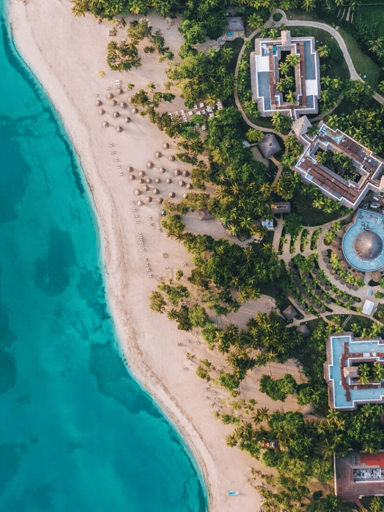 Tropical beach resort with lush greenery and luxury accommodations overlooking turquoise sea.