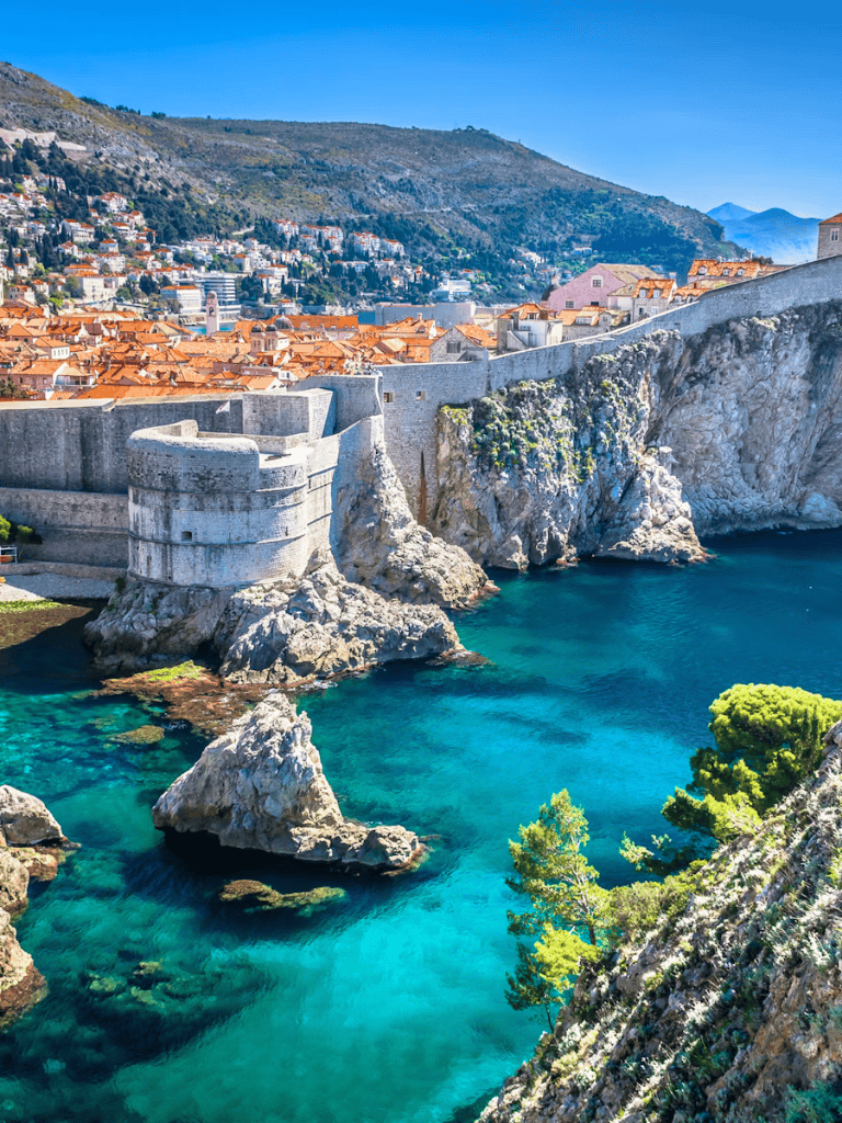 Vibrant coastal city with historic fortress, colorful rooftops, and turquoise waters along the rocky shoreline.