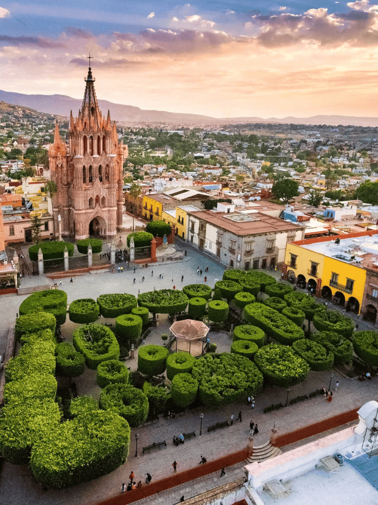 Colorful cityscape with historic pink church and lush green park at sunset.