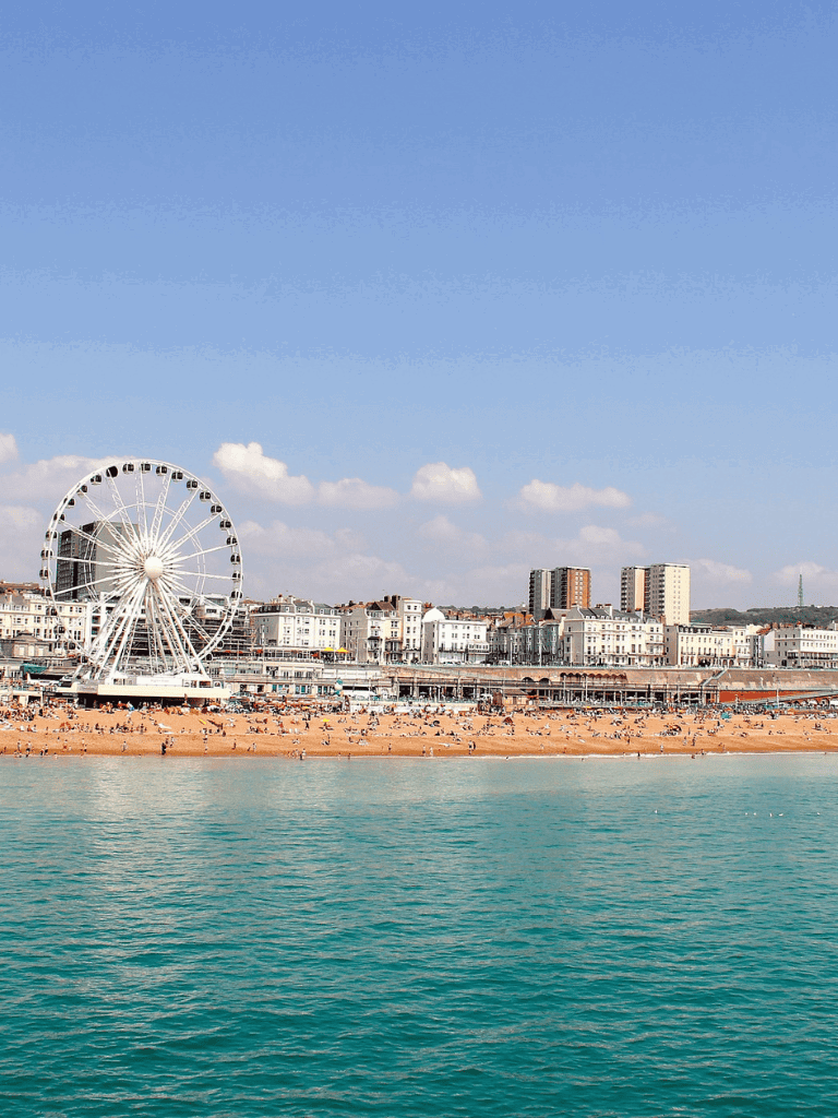 Bright Ferris wheel overlooking Brighton beach and city skyline in a scenic coastal setting.