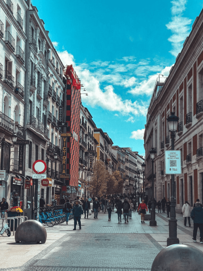 Madrid city street with historic buildings, pedestrians, and blue sky.