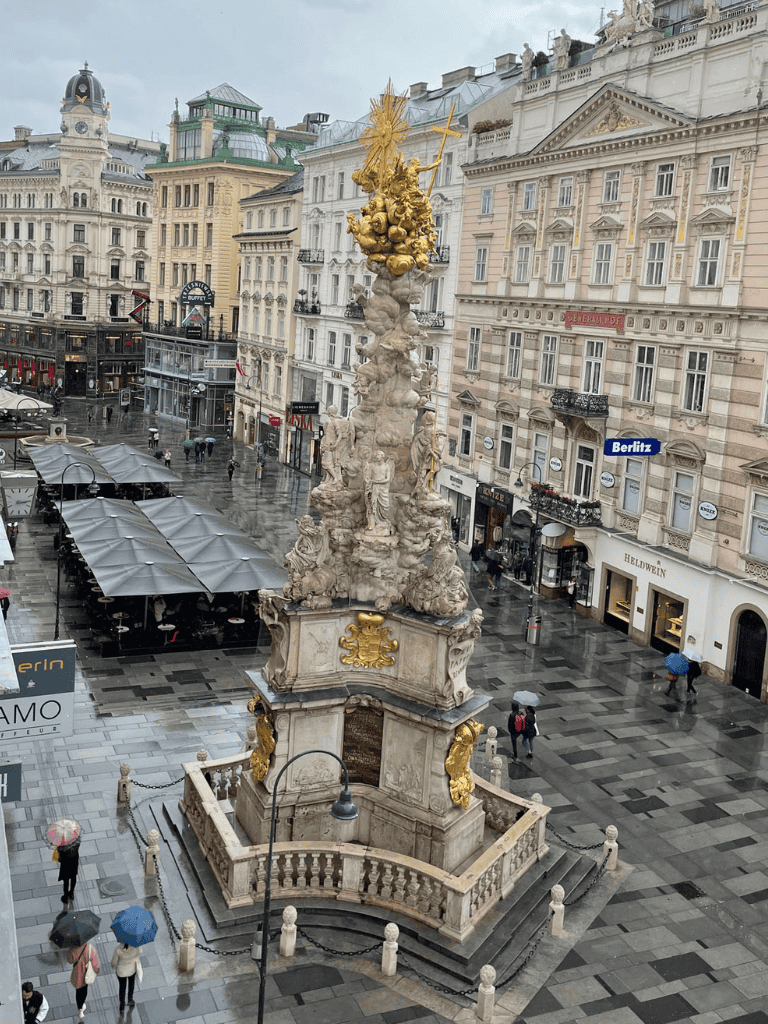 - Baroque city square monument with ornate sculptures and golden accents in rainy weather.
