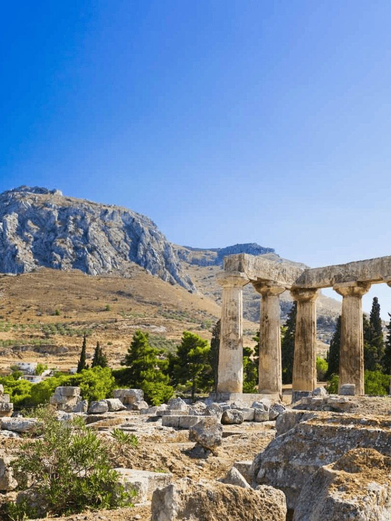 Ancient Greek ruins with mountains and clear blue sky in the background.
