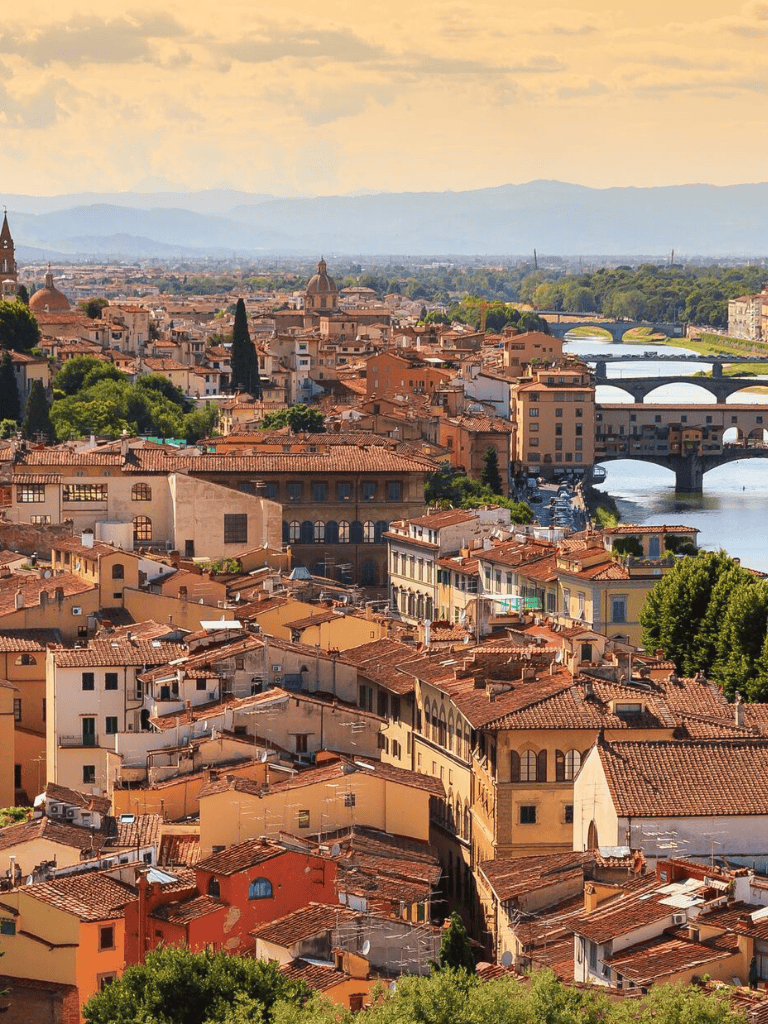 Historical Italian cityscape with terracotta rooftops and bridges over the river.