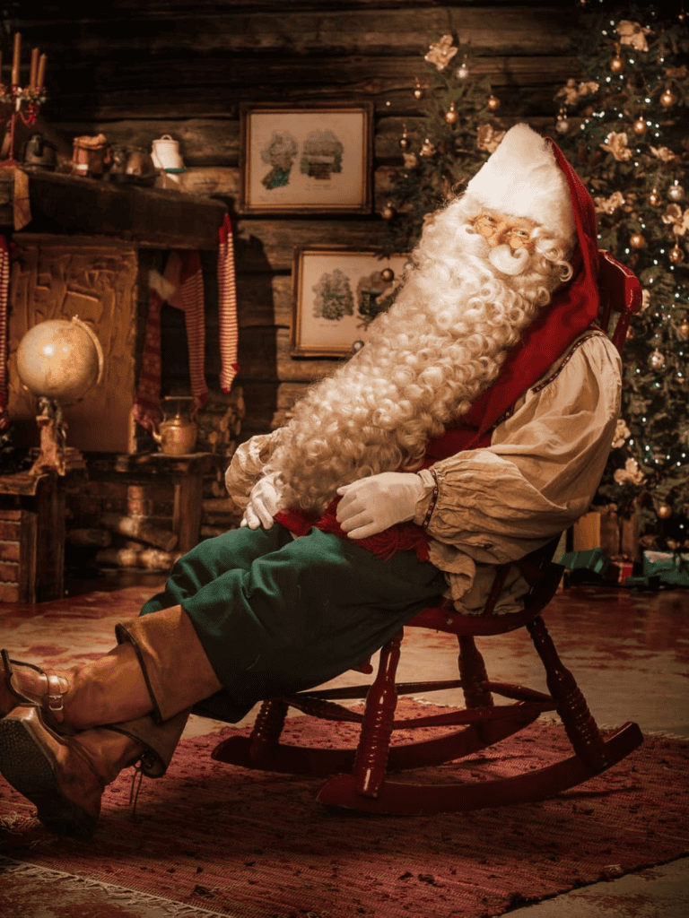 Santa Claus sitting on a rocking chair in a cozy Christmas cabin decorated with a Christmas tree and vintage ornaments.