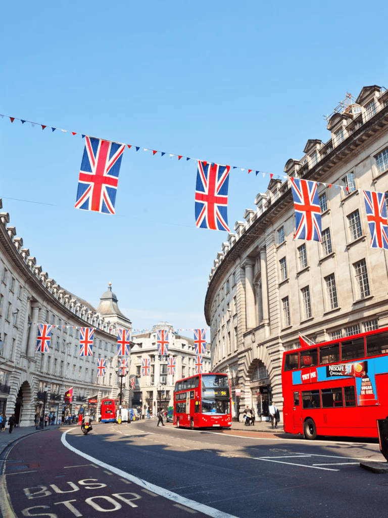 Union Jack flags decorating London streets, iconic red buses, historic architecture, popular UK travel destination.
