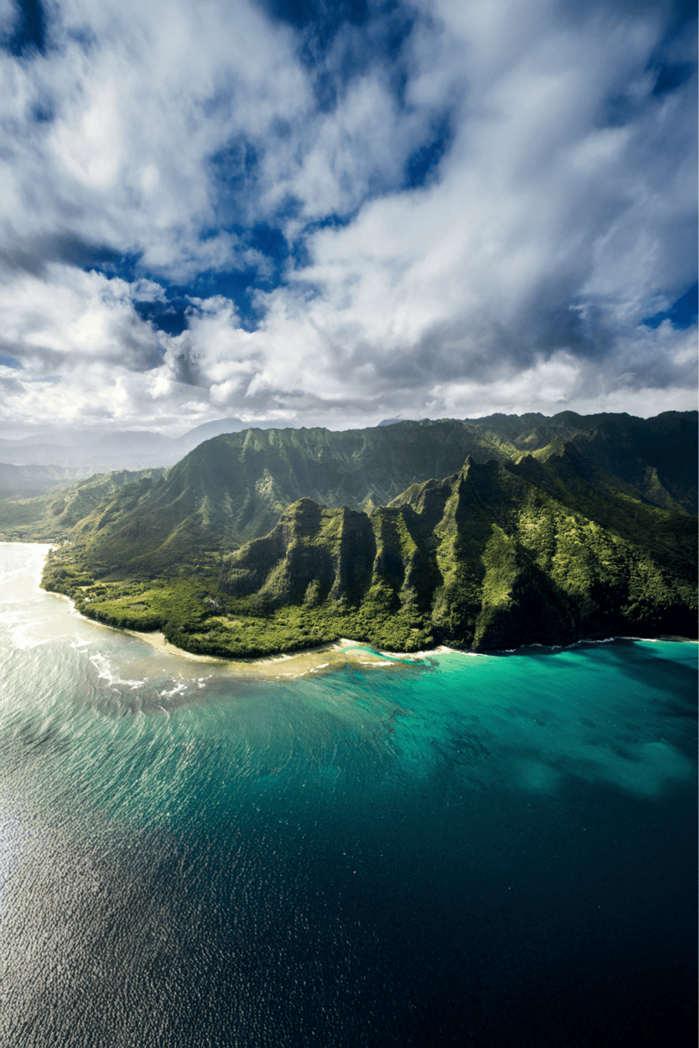 Lush green mountains and turquoise waters on an island landscape with dramatic clouds overhead.