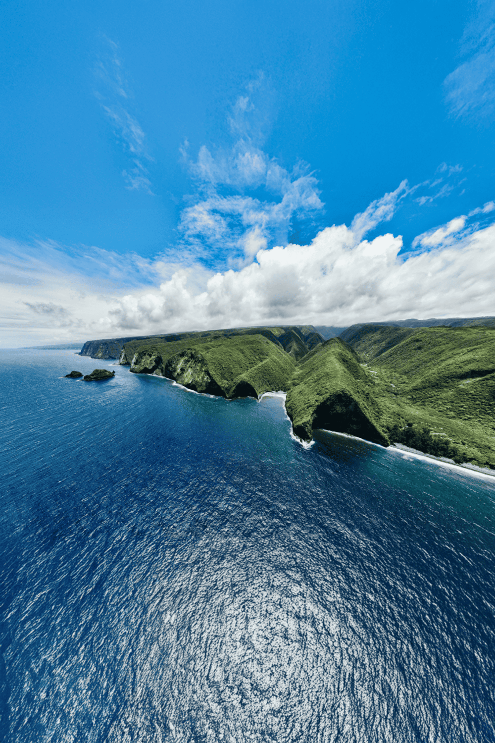 Breathtaking coastal cliffs with lush greenery and vibrant blue ocean under a partly cloudy sky.