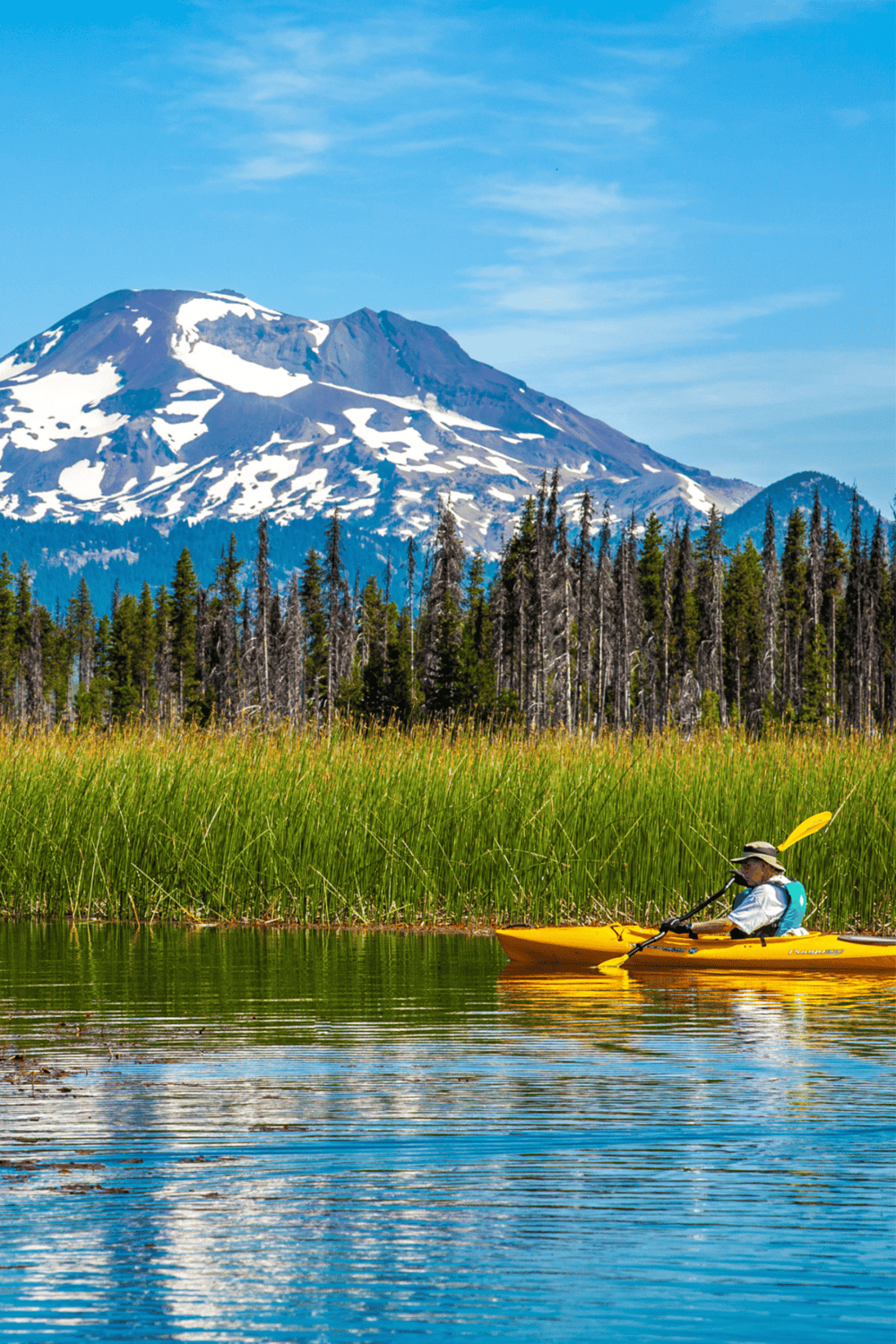 Serene kayaking near snow-capped mountains and lush forests, perfect for outdoor adventure enthusiasts.