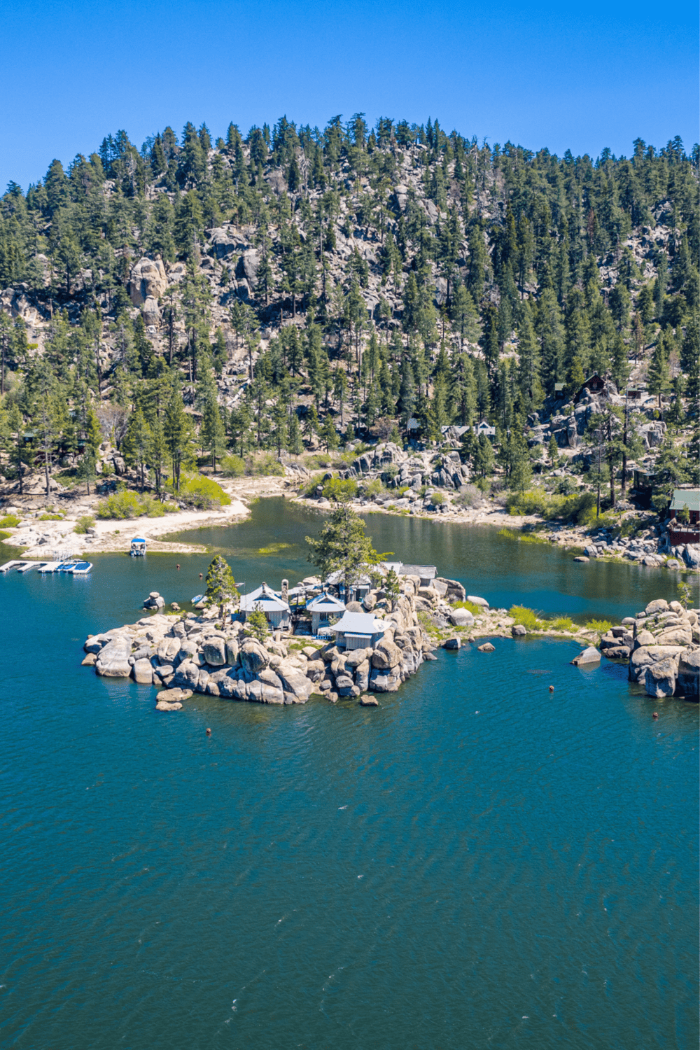 Serene mountain lake with small island and boats, surrounded by forest and rocky cliffs.