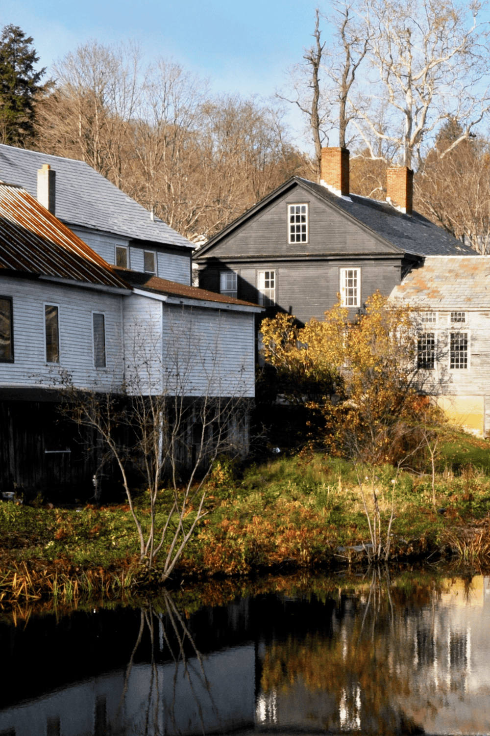 Rustic houses with fall foliage reflection by the water, scenic rural landscape in autumn.