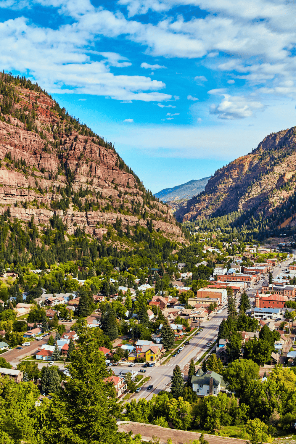 Remote mountain town nestled in lush green valley with red rocky cliffs, ideal for travel planning and outdoor adventures.
