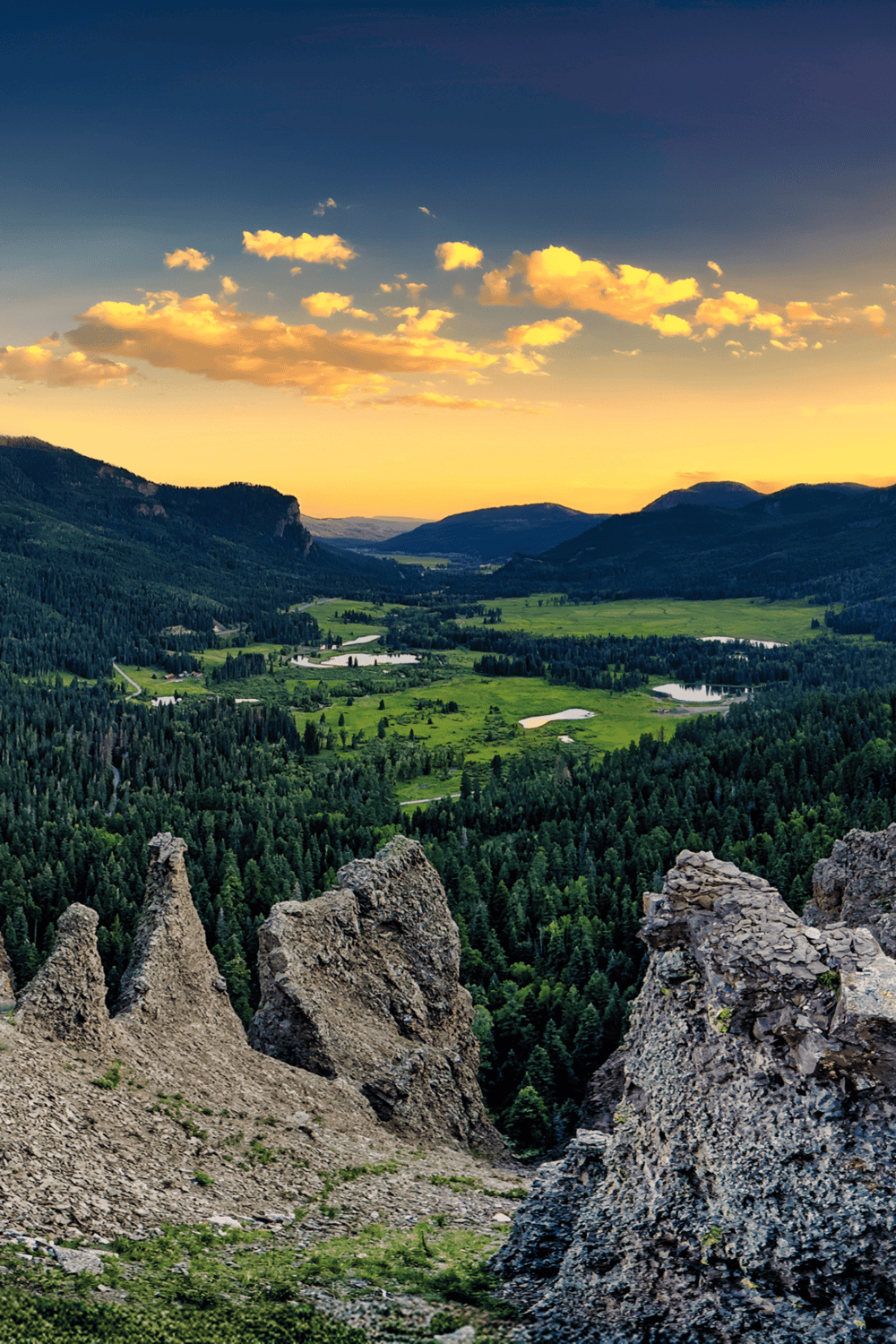 Vibrant mountain valley landscape at sunset with lush greenery and rocky formations.