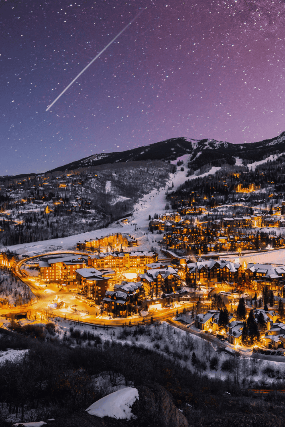 Night ski resort illuminated in the mountains under a starry sky and shooting star.