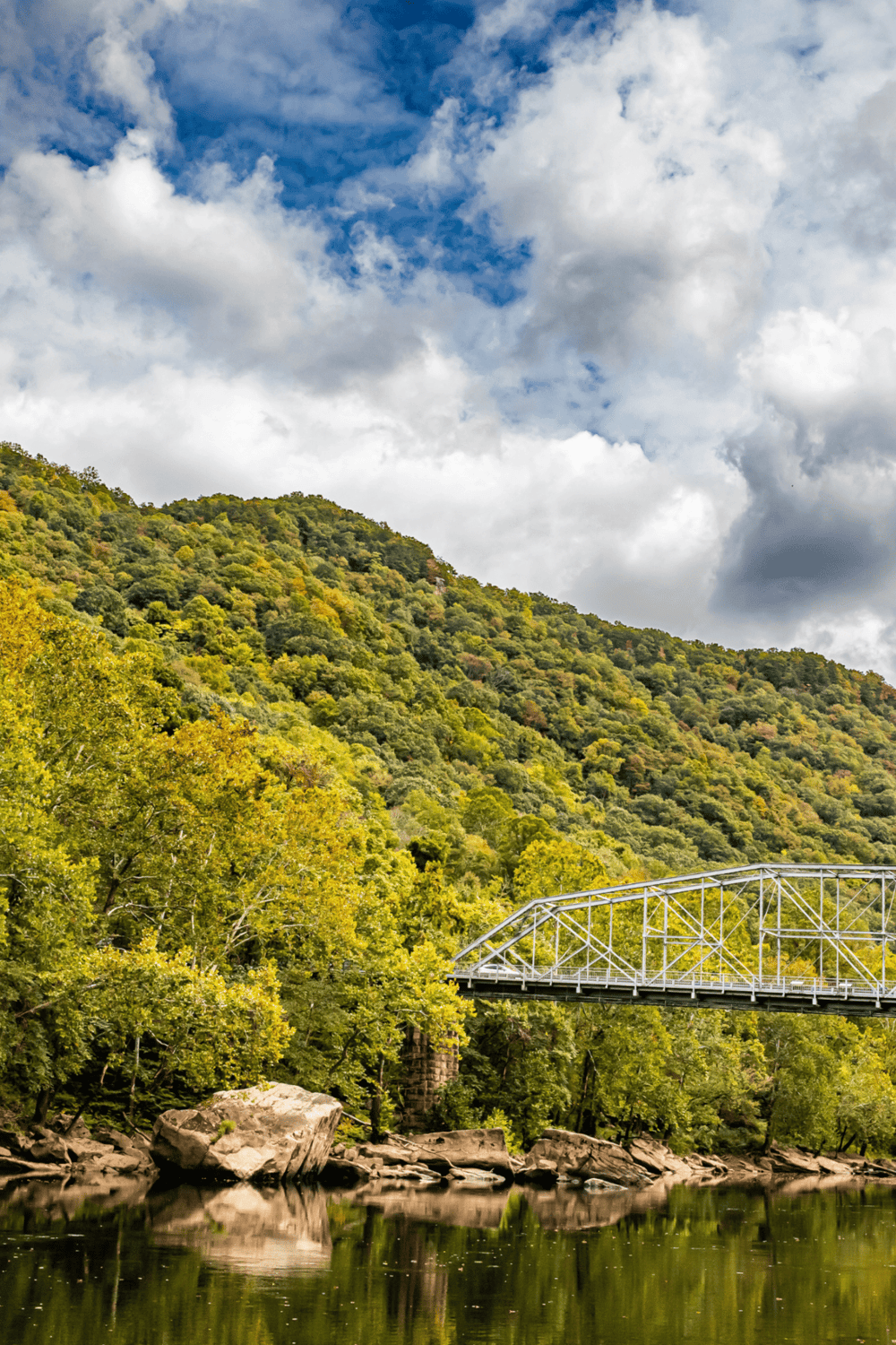 Serene landscape featuring a scenic river, lush green hillside, and a bridge under a cloudy sky, ideal for travel and outdoor adventure content.