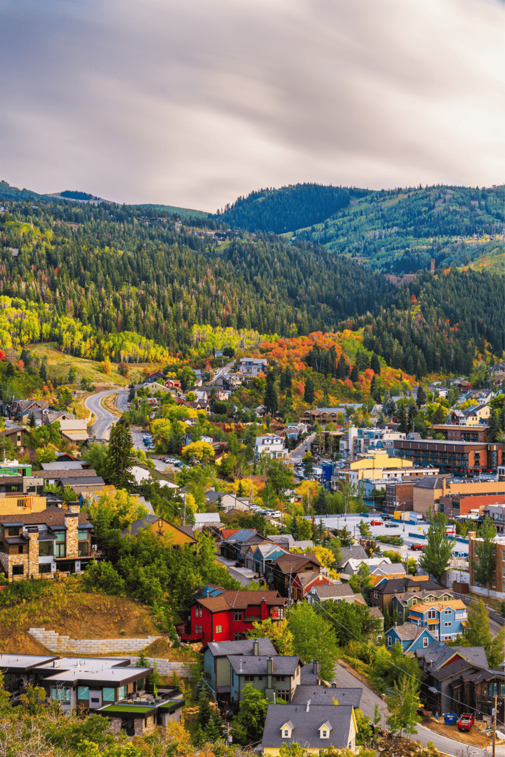 Colorful mountain town with vibrant houses and lush forested hills under a cloudy sky.