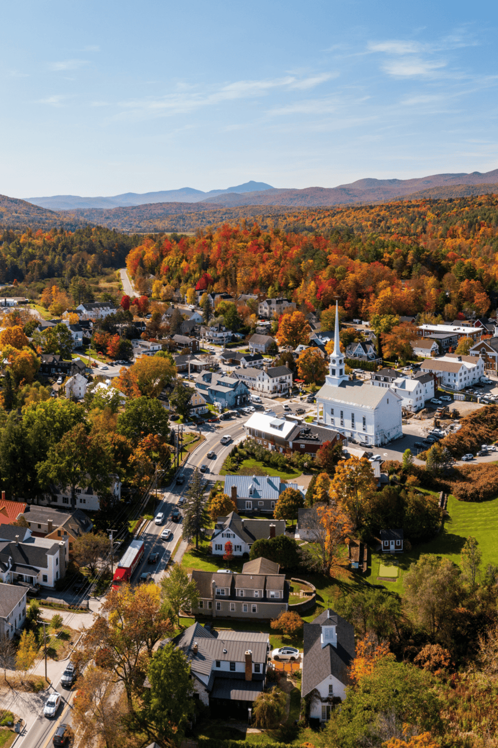 Colorful autumn town with church, surrounded by fall foliage and mountain views.
