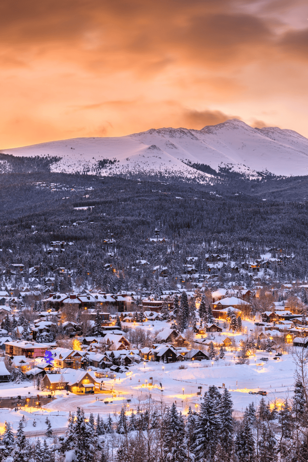 Snowy mountain village during sunset with glowing lights and winter landscape.