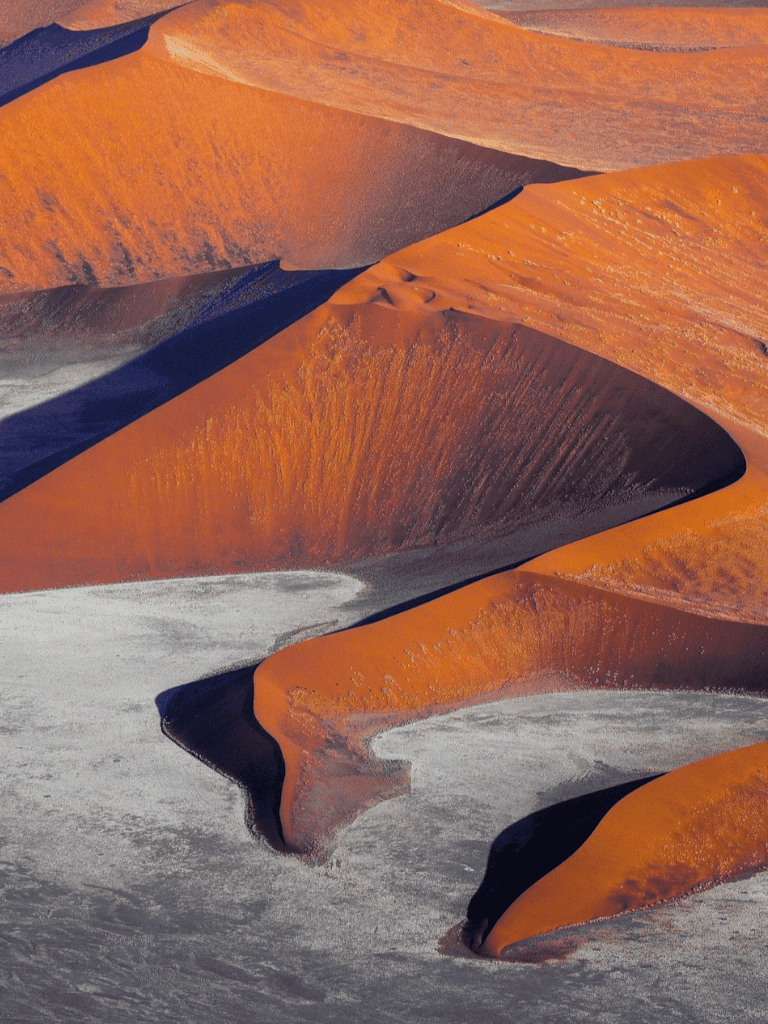 Orange sand dunes in a desert landscape with striking shadows and patterns.