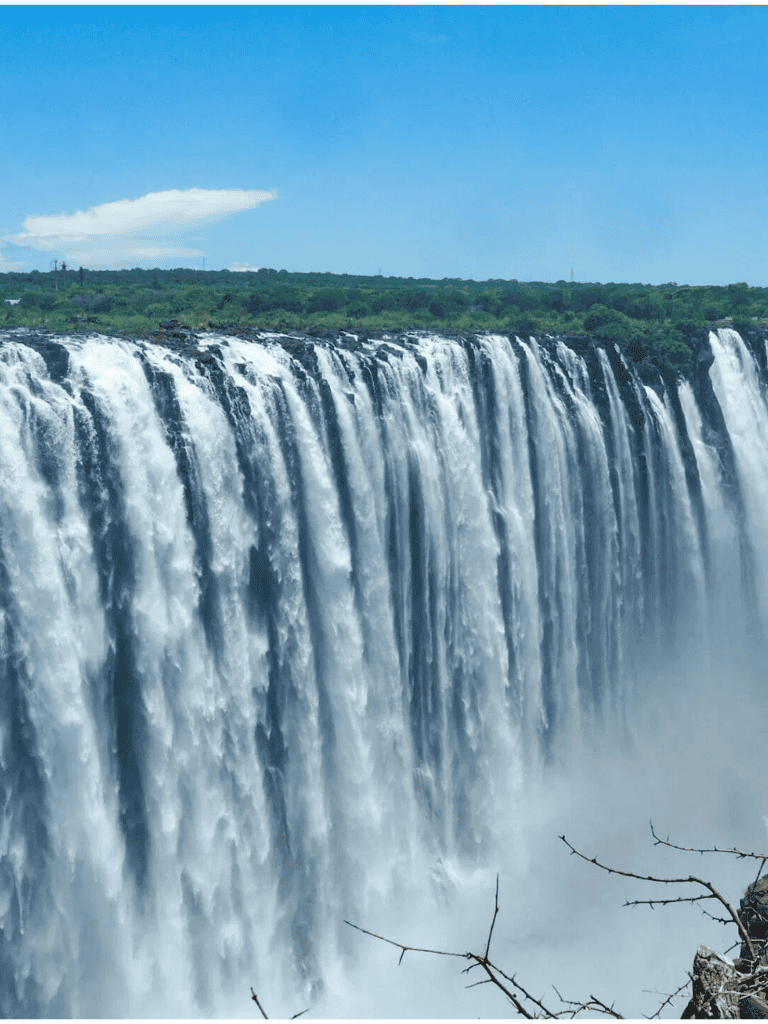 Vibrant waterfall with lush green landscape and blue sky in the background.