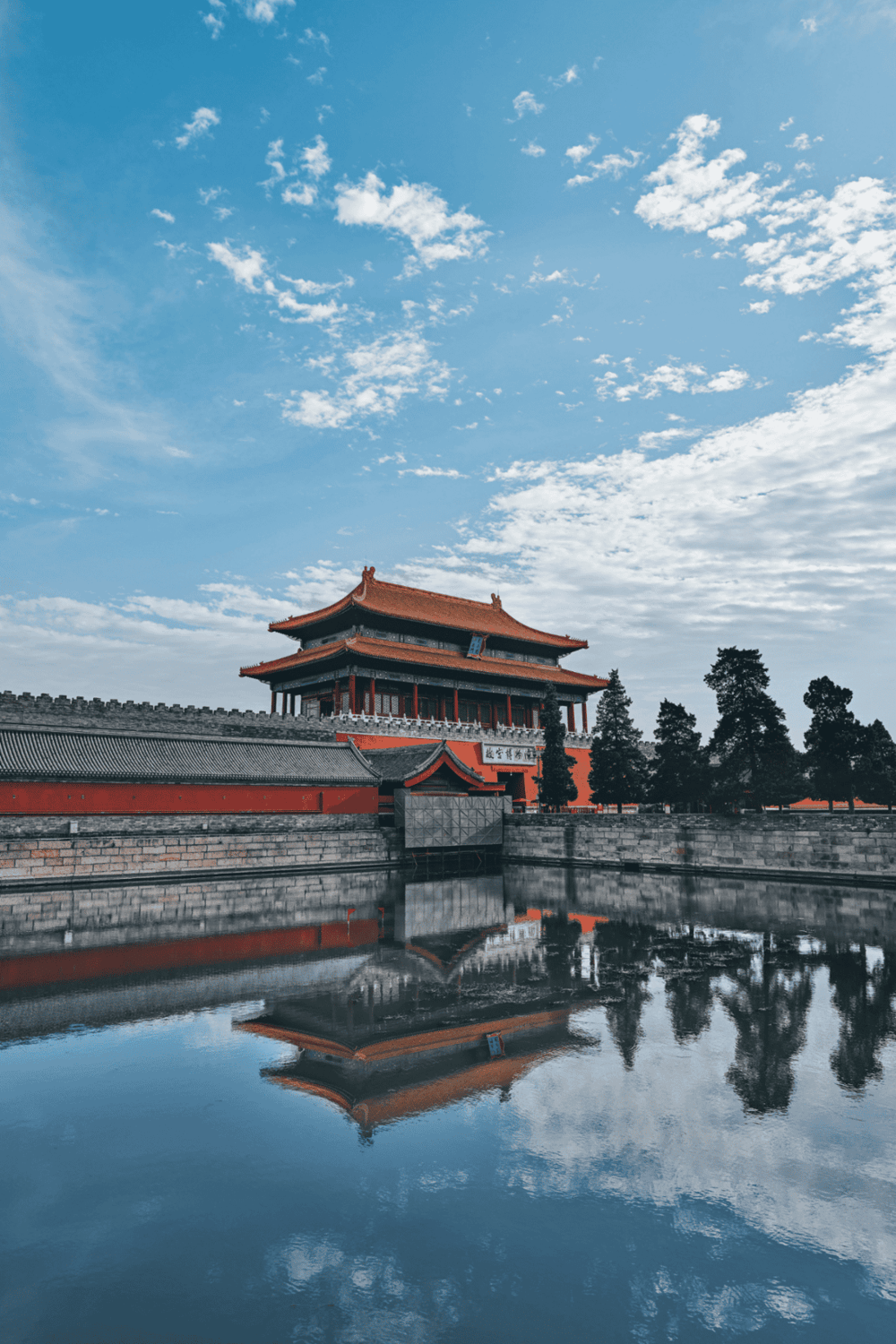 Ancient Chinese architecture with a traditional building reflected in water under a blue sky.