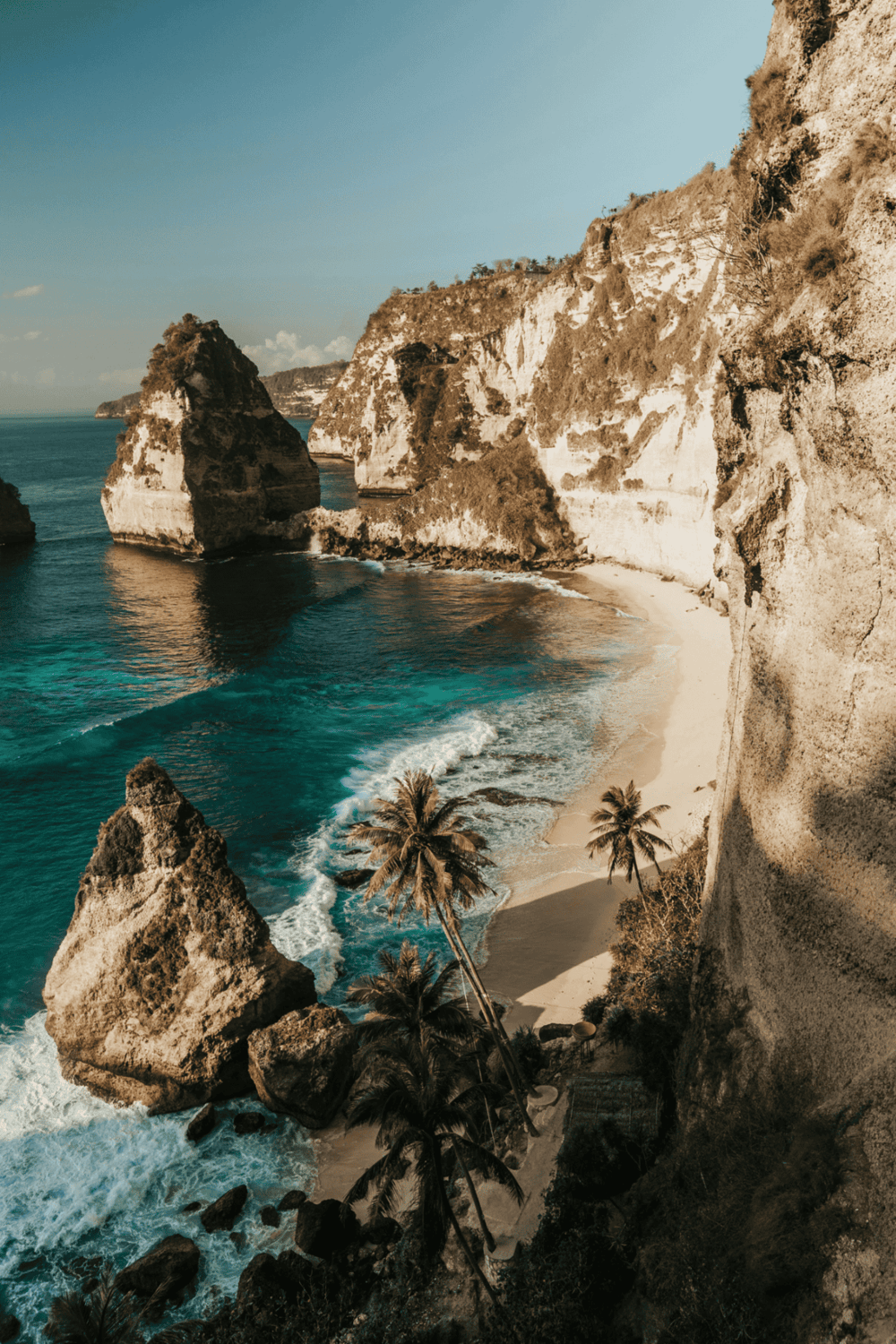 Secluded beach with dramatic cliffs and palm trees, perfect for relaxing and sightseeing in Bali.