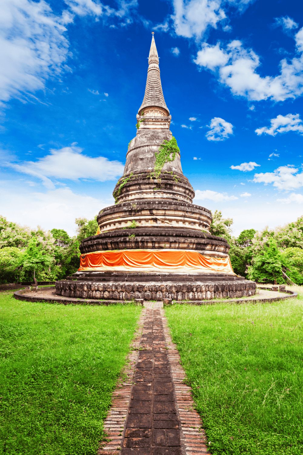 Ancient pagoda in lush green park under blue sky, a serene travel destination in Thailand.