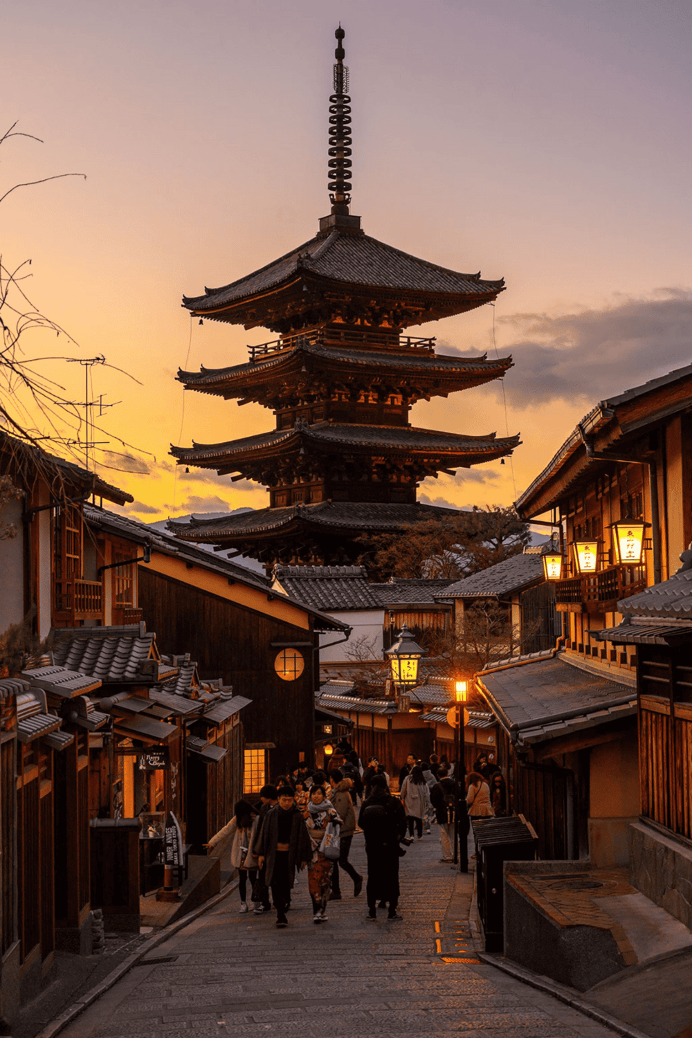 Ancient Japanese pagoda at sunset in historic Kyoto street with traditional shops and lanterns.
