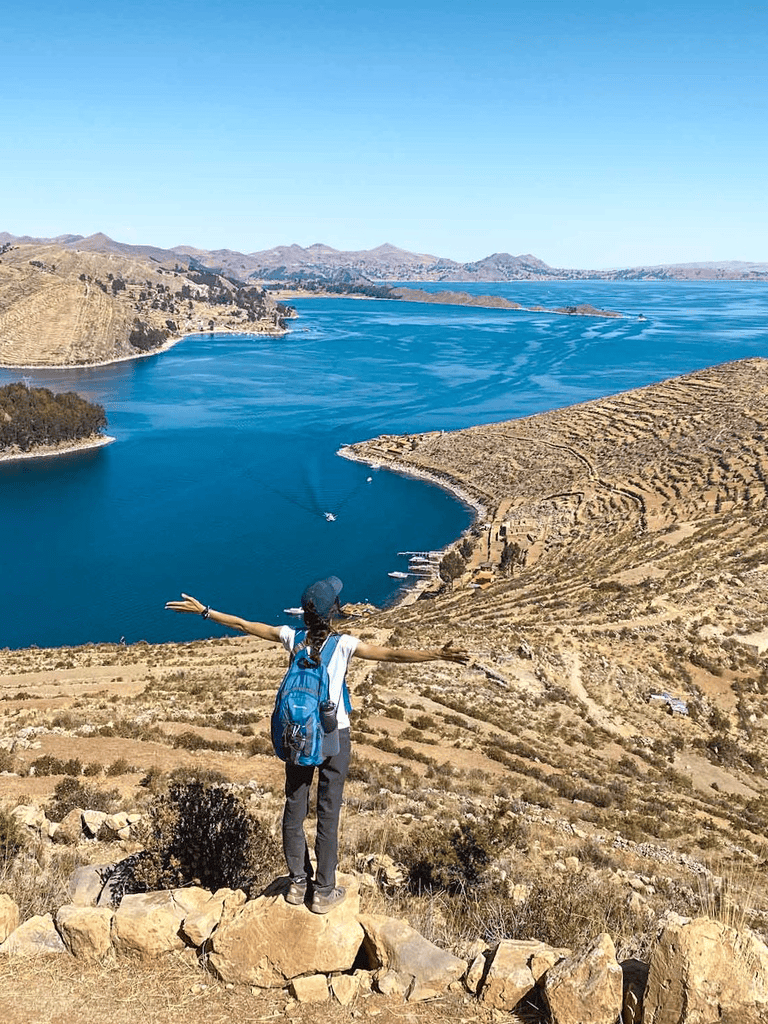 Breathtaking view of a woman enjoying nature at a scenic lake with mountains in the background.