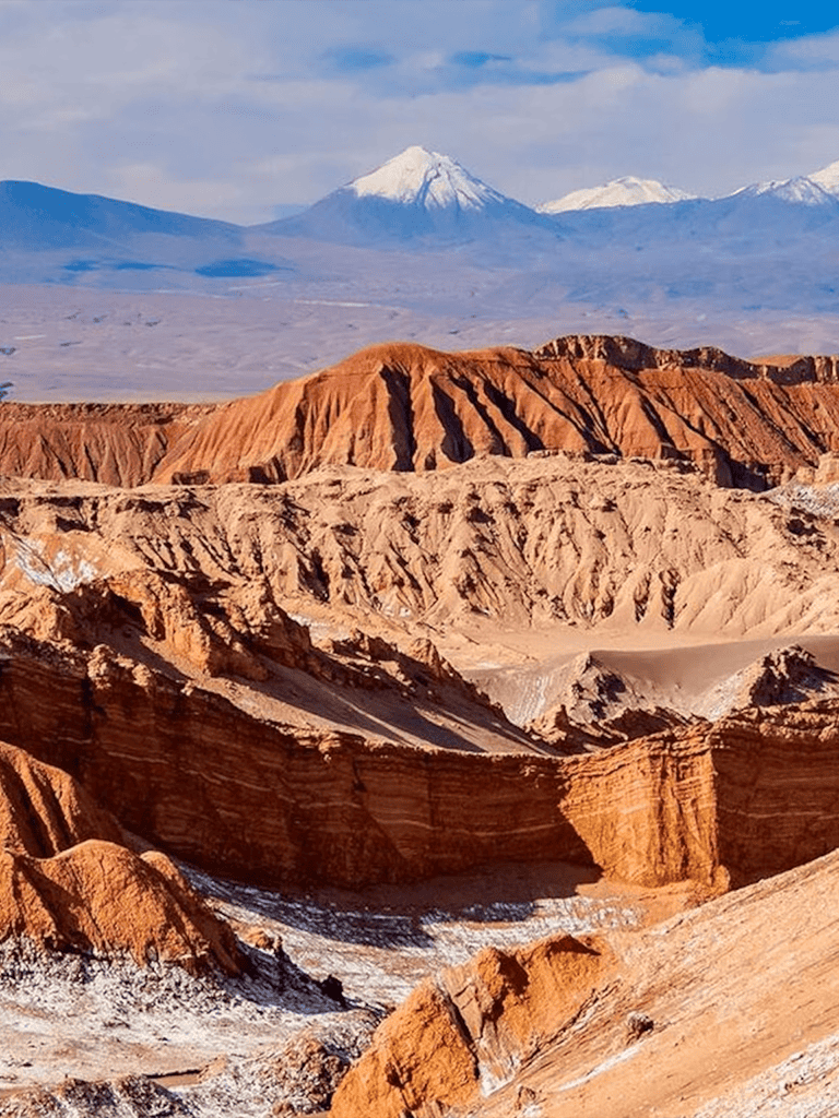 Vibrant desert landscape with colorful rock formations and snow-capped mountains in the background.