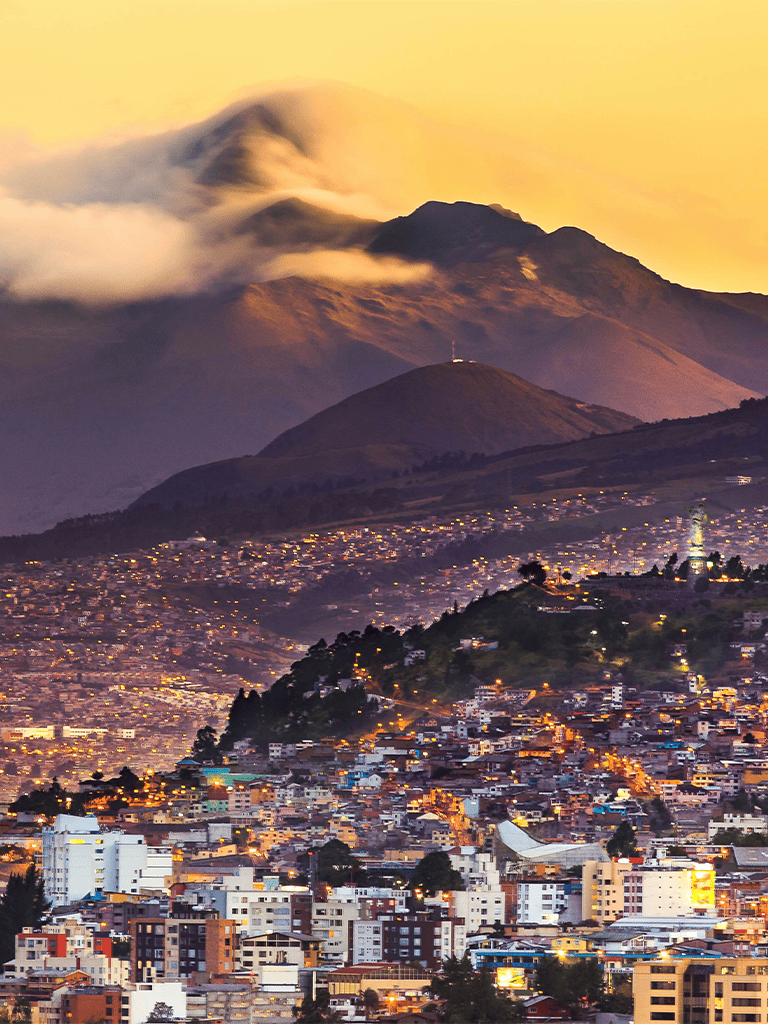 Vibrant cityscape with mountain backdrop at sunset, showcasing urban development near volcanic mountains.