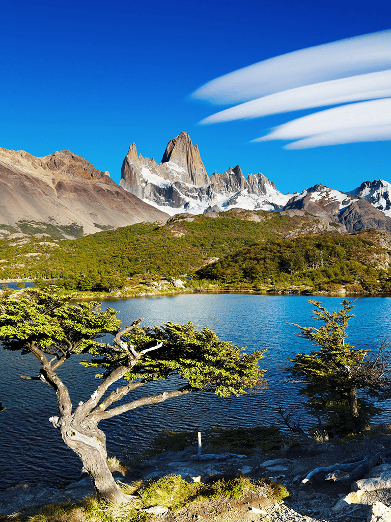 Spectacular Patagonian mountain landscape with lake, lush greenery, and unique cloud formations in Torres del Paine National Park.