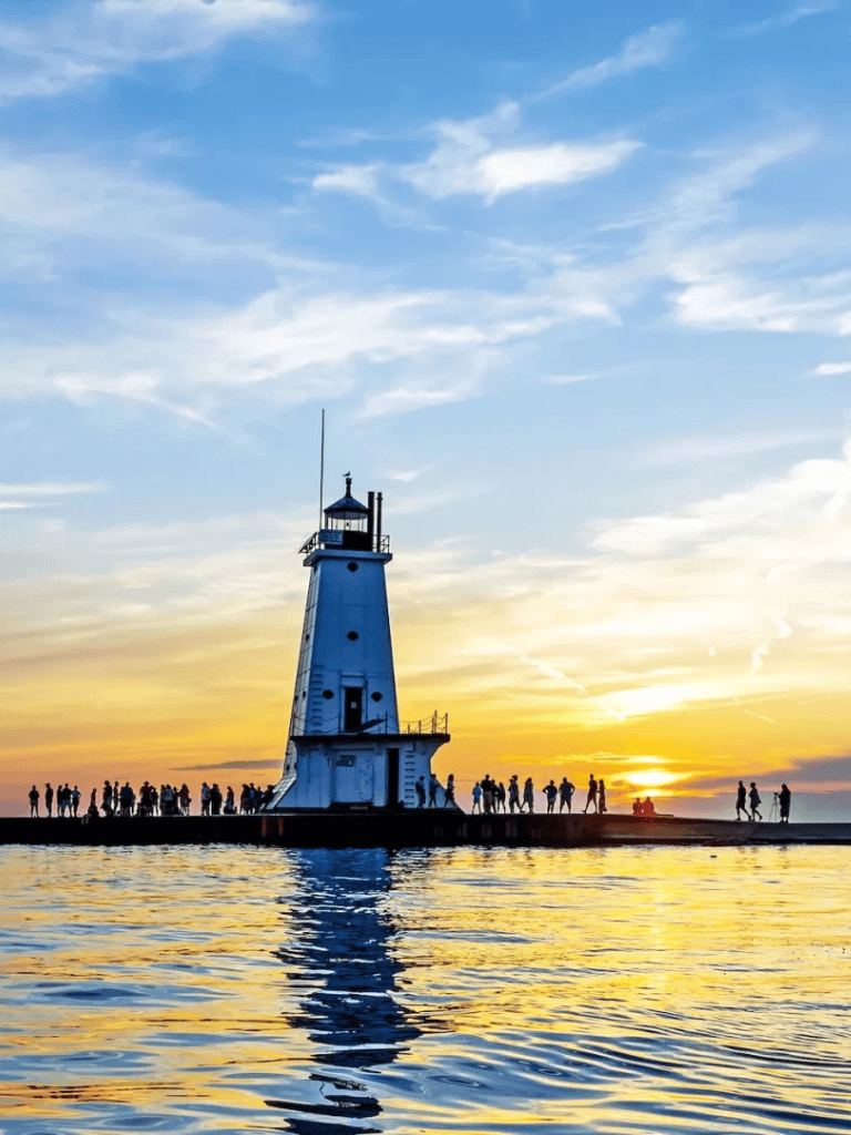 Lighthouse at sunset on Lake Michigan with people enjoying the scenic view.