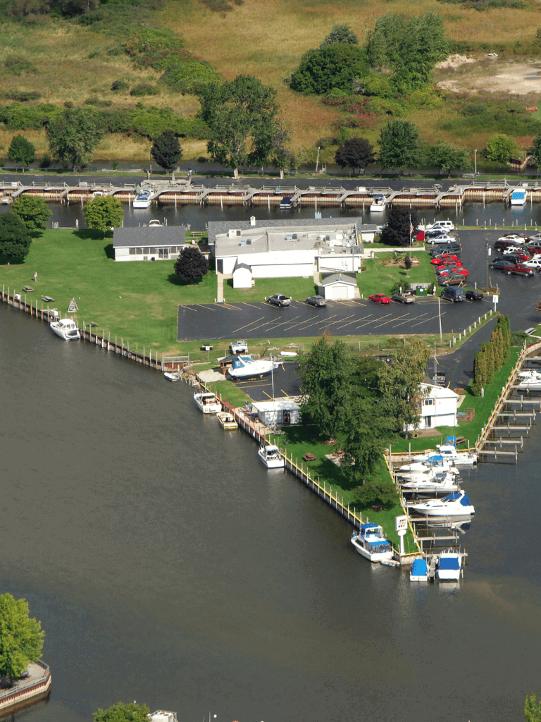 Marina with boats docked along waterfront and parking lot overlooking river and scenic landscape.
