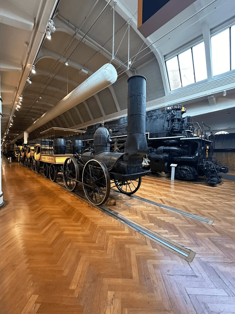 Old steam locomotive and vintage train exhibit in a museum indoor setting.