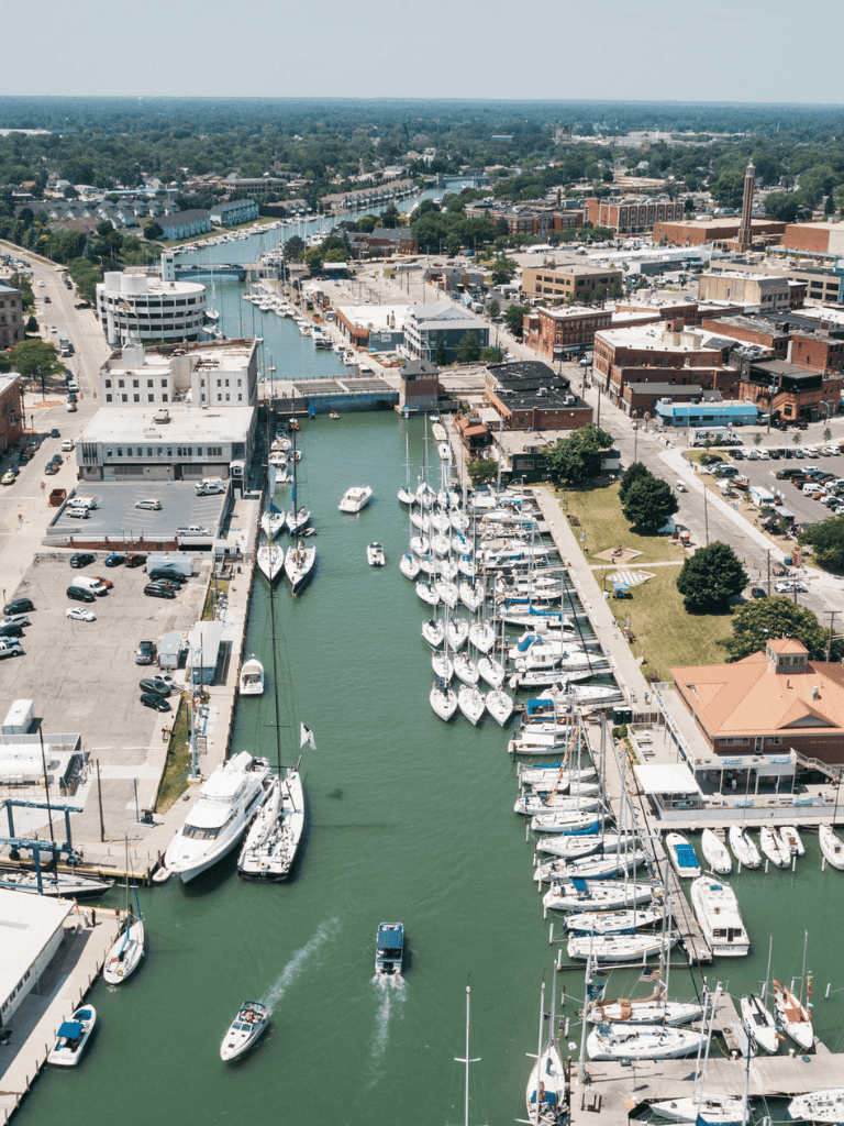 Charming marina harbor with boats, shops, and town buildings seen from aerial view.