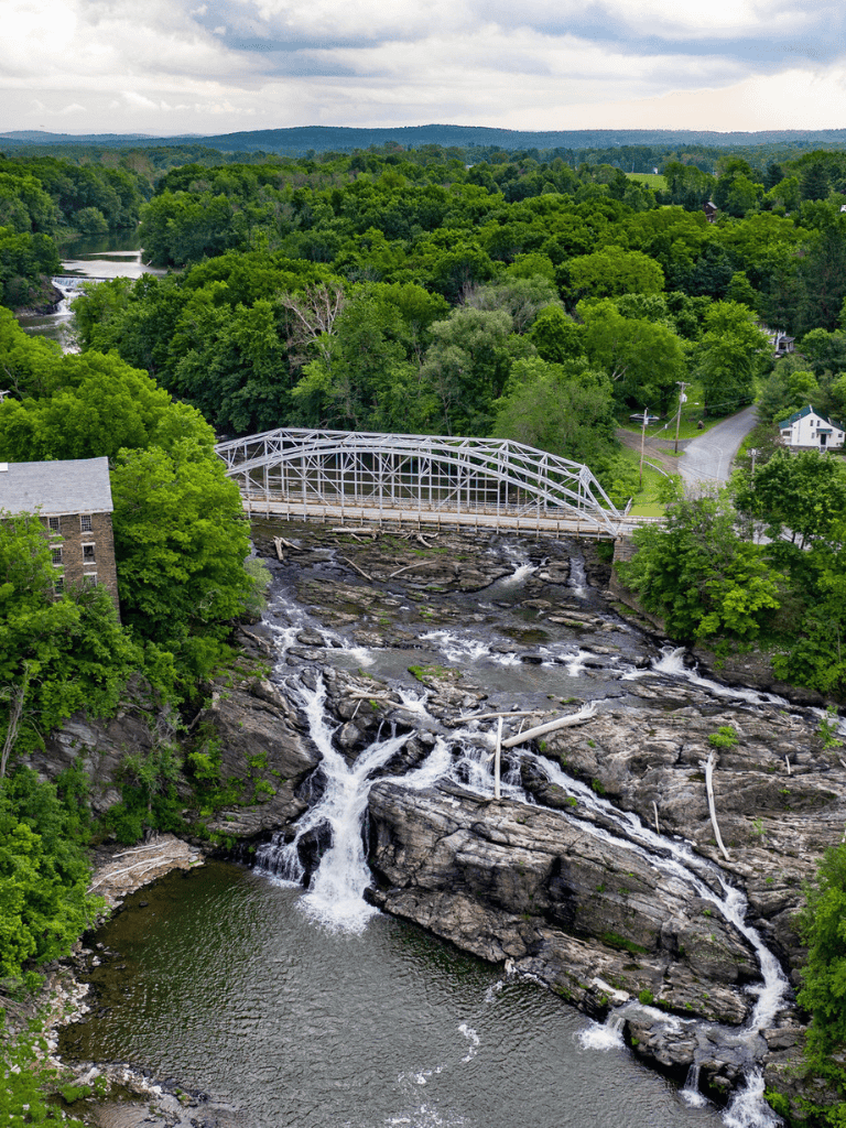 Lush green landscape with a waterfall and a bridge over a river, scenic countryside view.