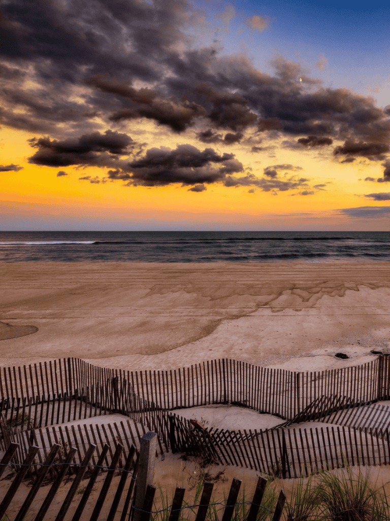 Seaside beach sunset with dramatic clouds and sand dunes, scenic coastal landscape for travel and vacation planning.