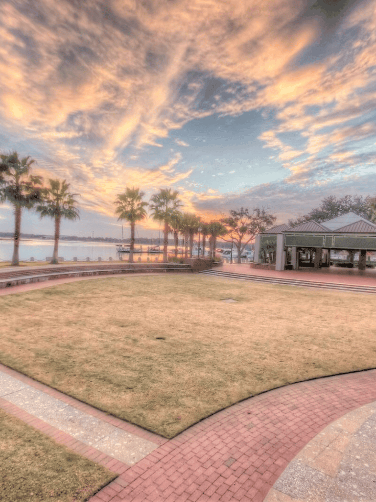 Vibrant sunset over lakeside park with palm trees and walking paths, ideal for outdoor recreation and relaxing scenery.