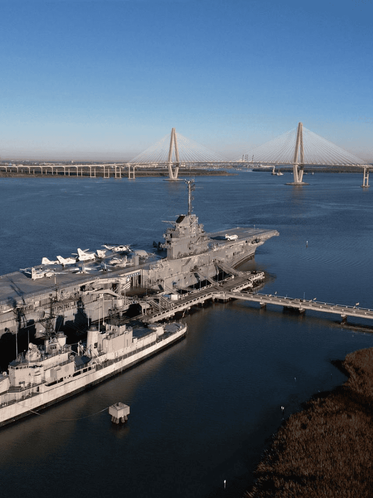 Aircraft carrier docked at port with bridge in background.