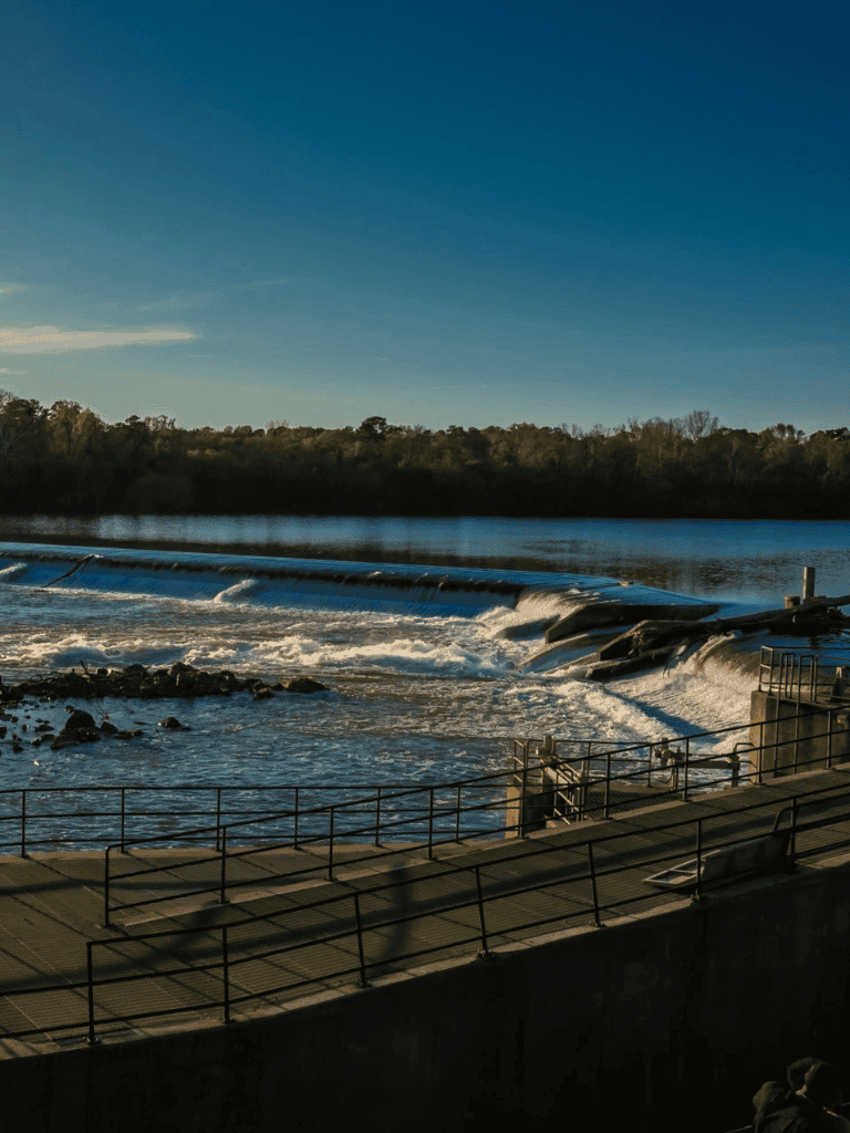 Riverside dam with spillway, scenic water flow, nature landscape, peaceful waterway, outdoor natural scenery, QuestForDirections.