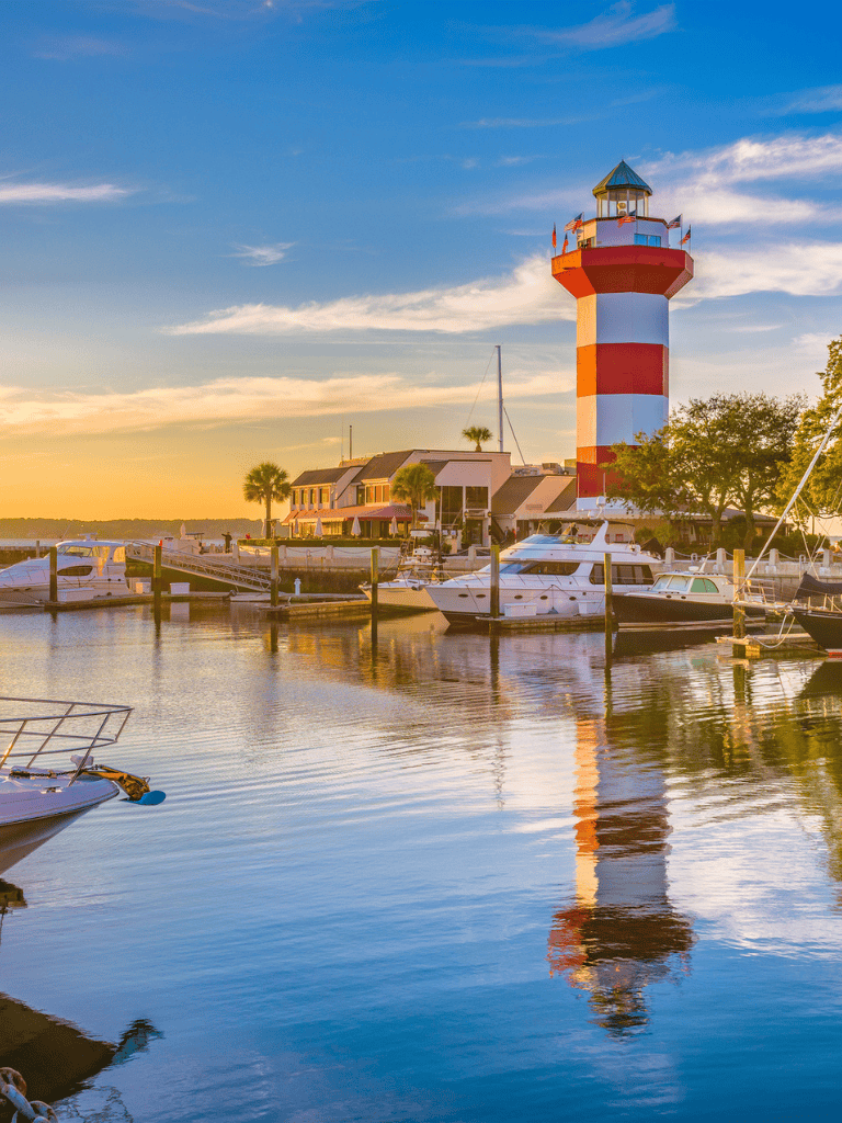 Colorful lighthouse at dusk near marina with boats, waterfront dining, and scenic sunset views in Florida.