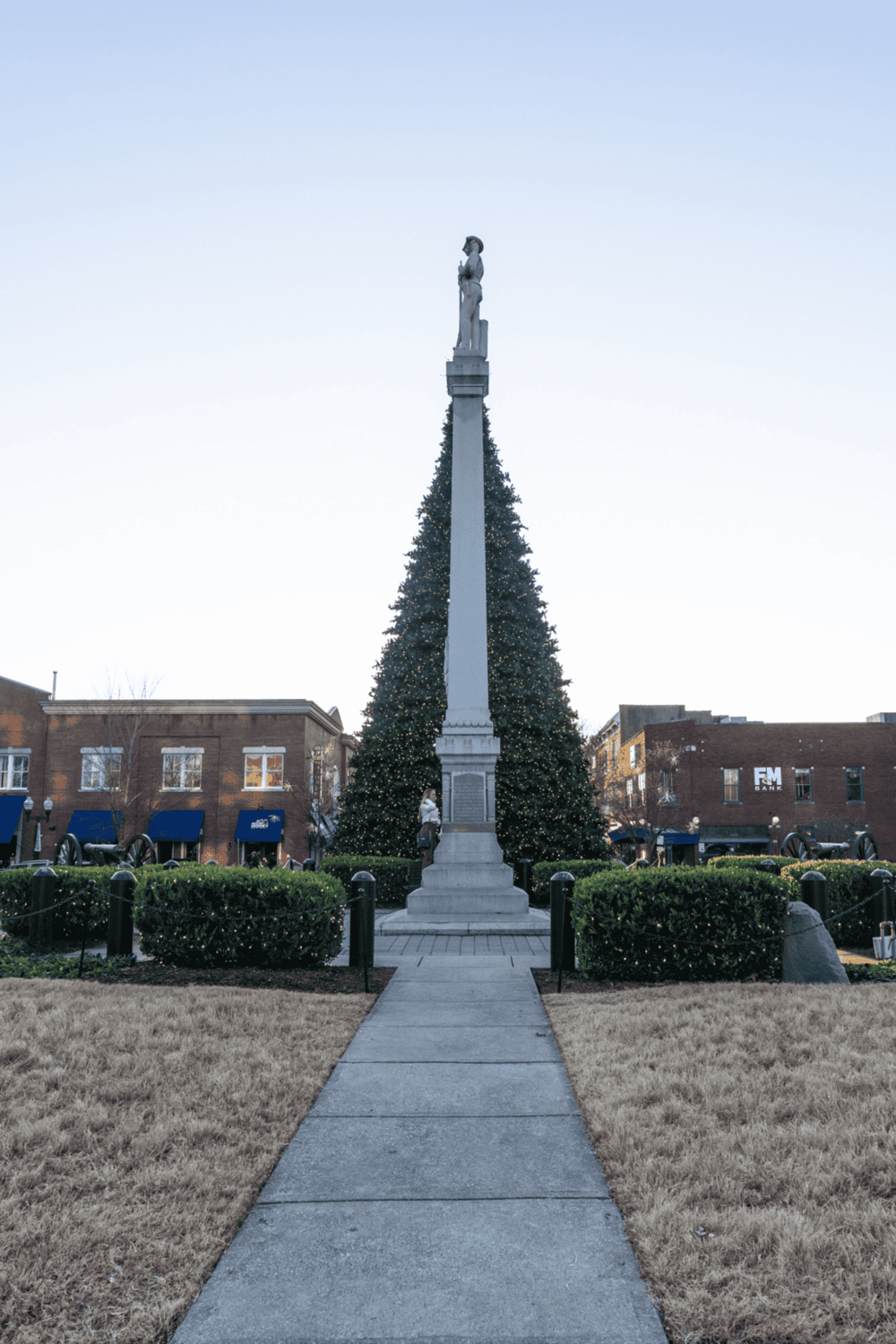 Historical monument with Christmas tree in city square, festive holiday decor, and urban surroundings.
