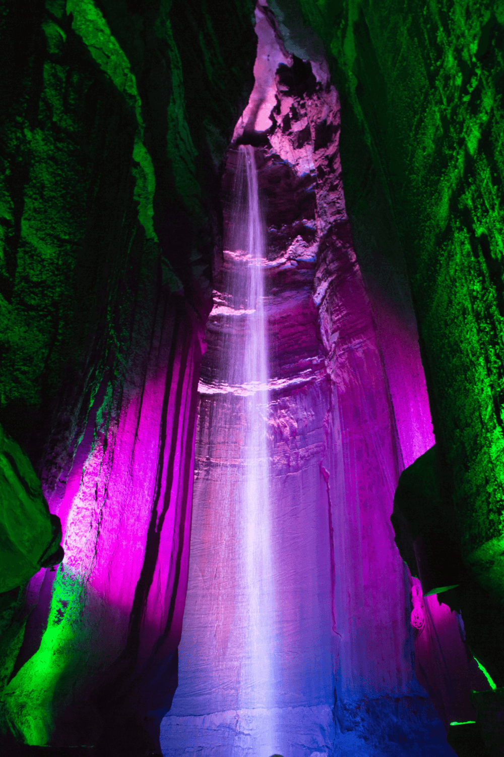 Colorful illuminated waterfall in a narrow canyon with green and purple lights.