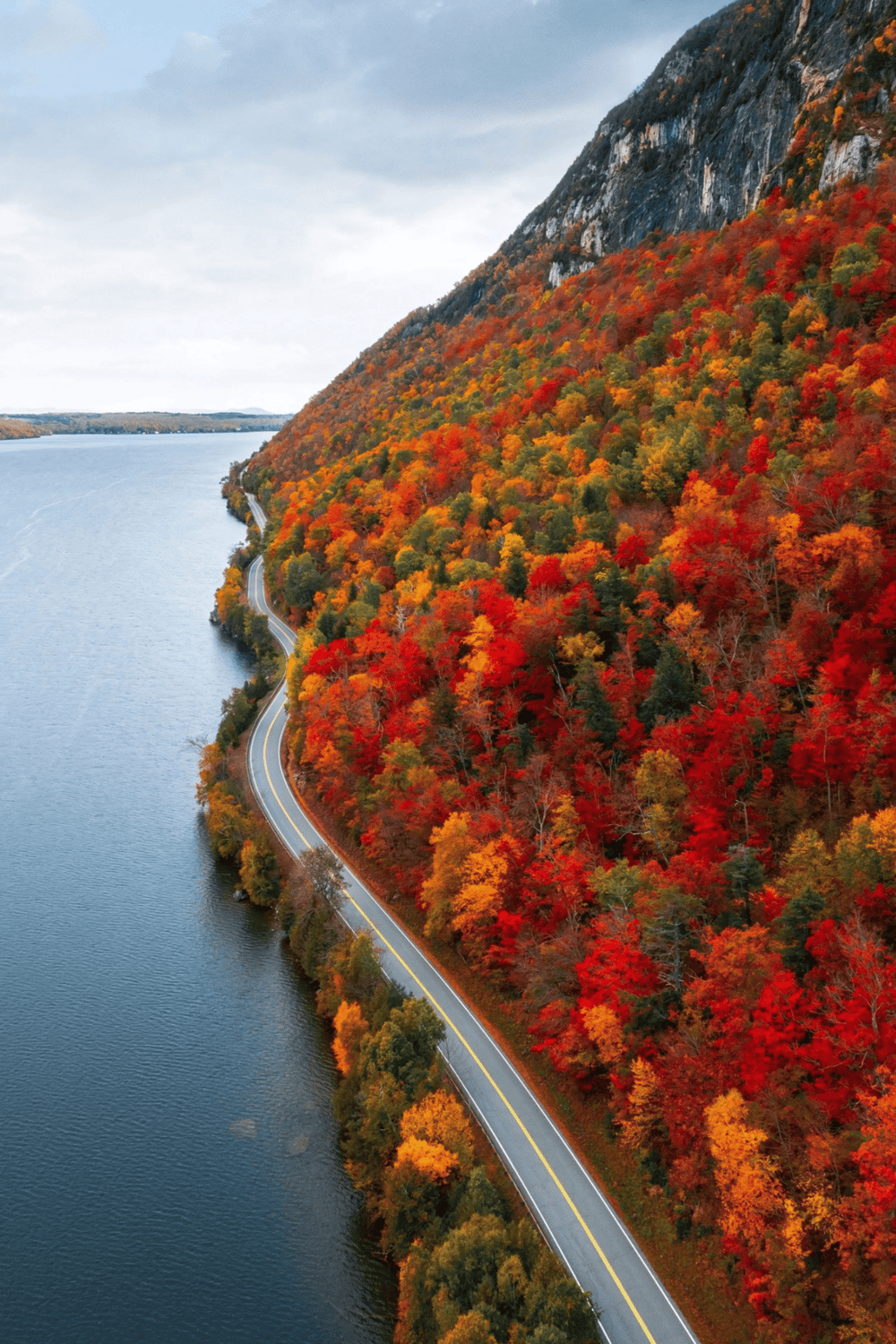 Colorful fall foliage along winding mountain road by lake.