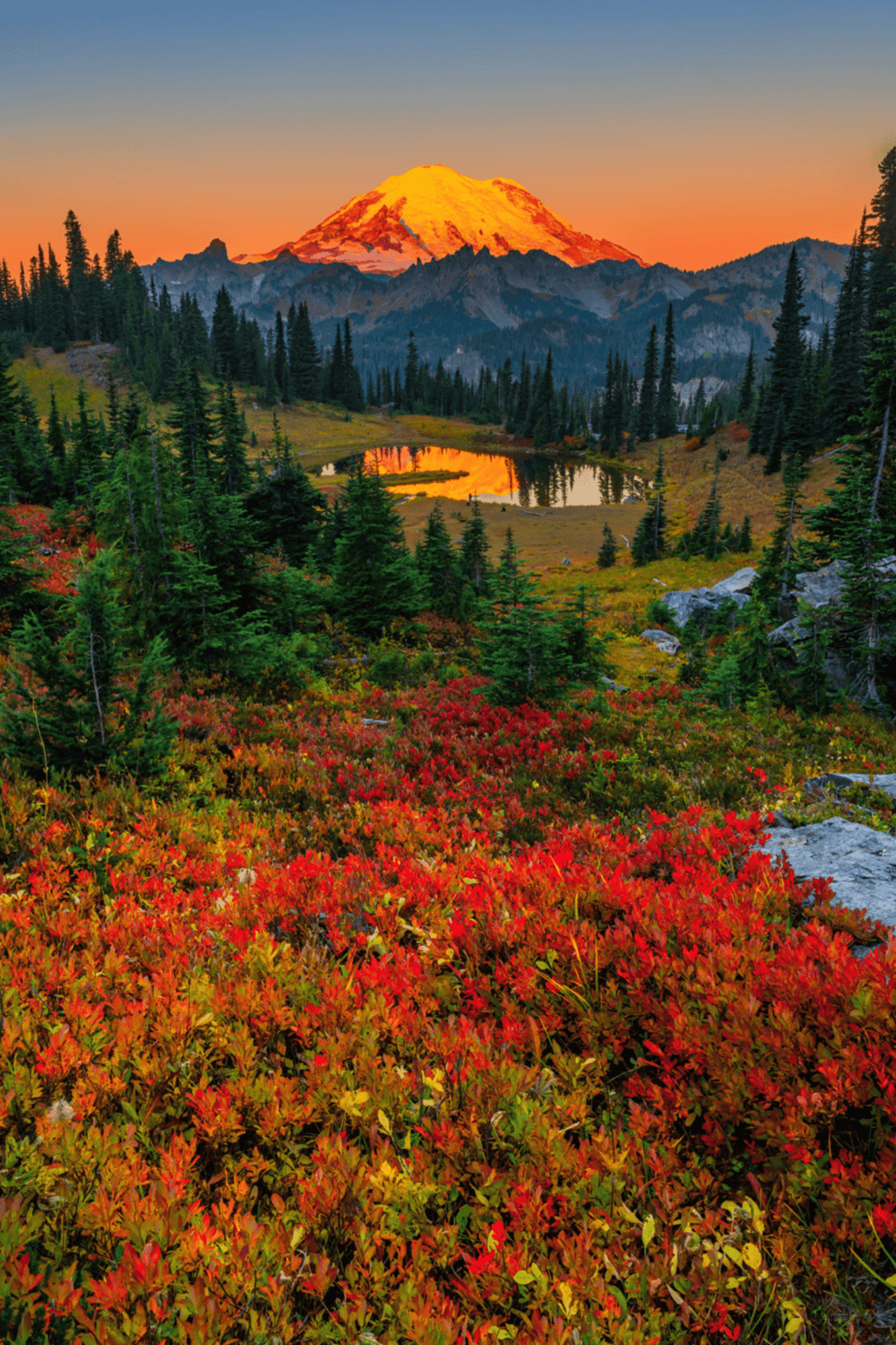 Vibrant autumn foliage surrounding a serene mountain lake with Mount Rainier in the background.